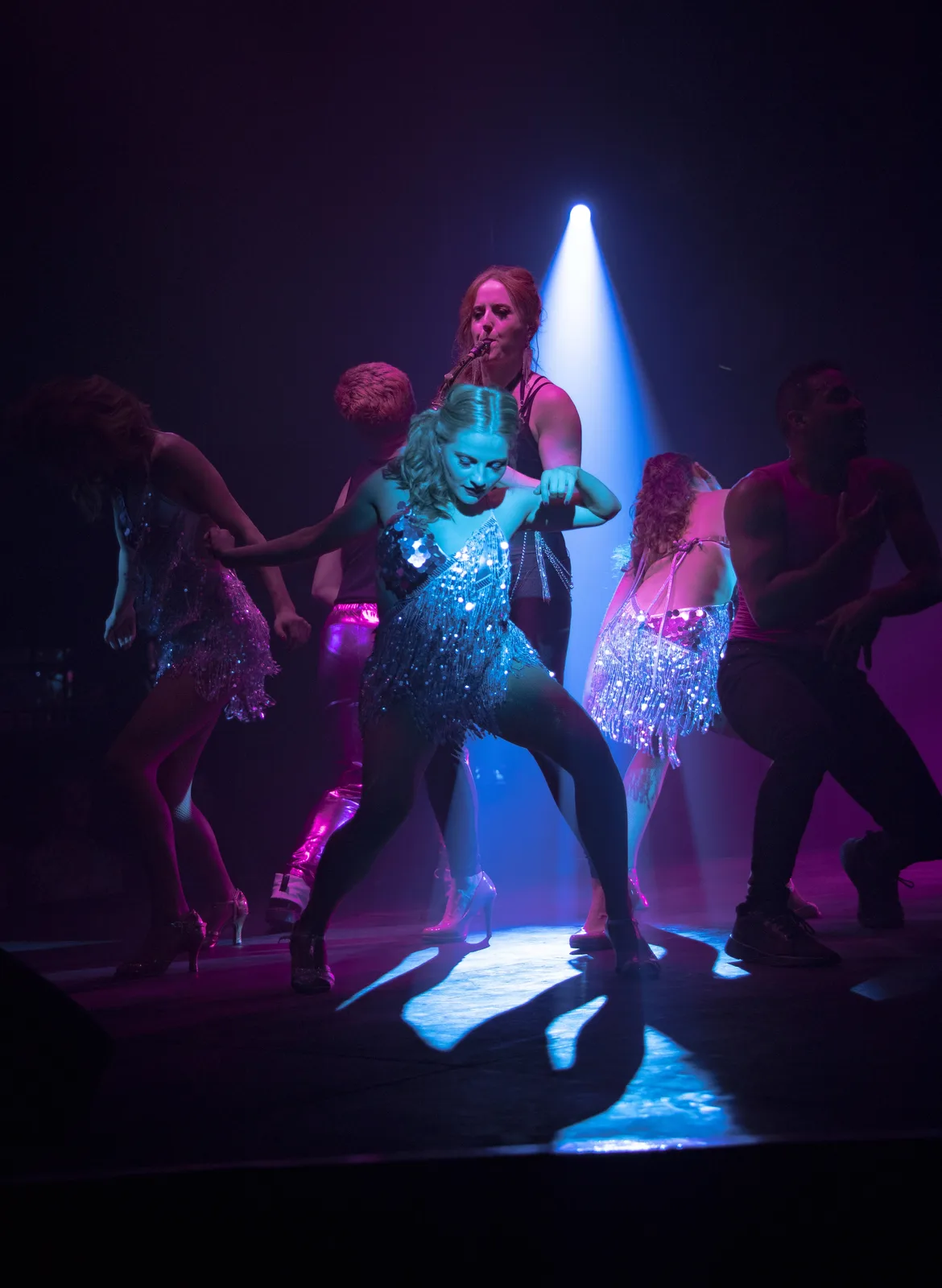 Sarah Saxophone performing on stage with dancers under blue stage lighting at a corporate event