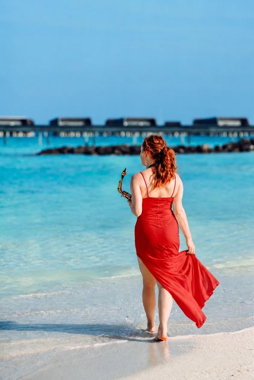 Sarah Saxophone walking along a tropical beach in a red dress holding her saxophone for an international destination performance
