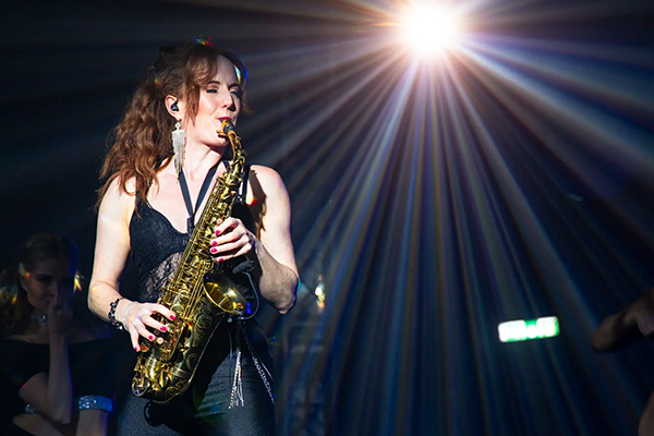Sarah Saxophone performs in front of a bright light in a club